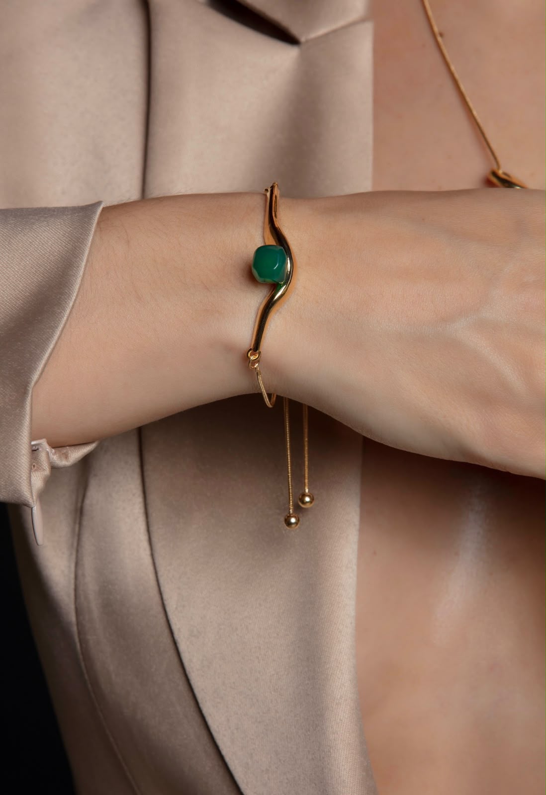Bracelete dourado com pedra verde esmeralda no pulso